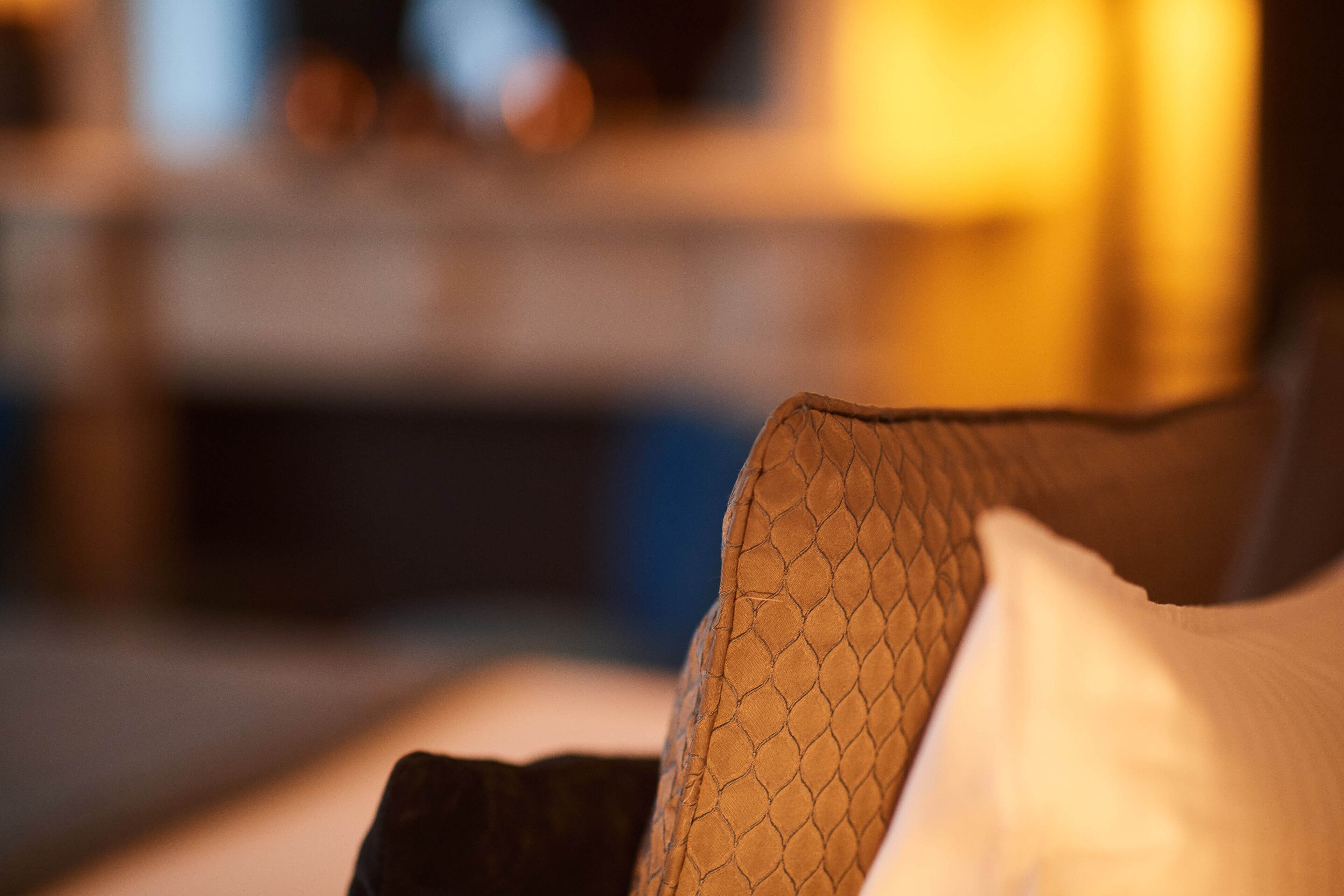 A close-up of a textured fabric, possibly a part of a bed or couch, with a blurred background suggesting an indoor setting.