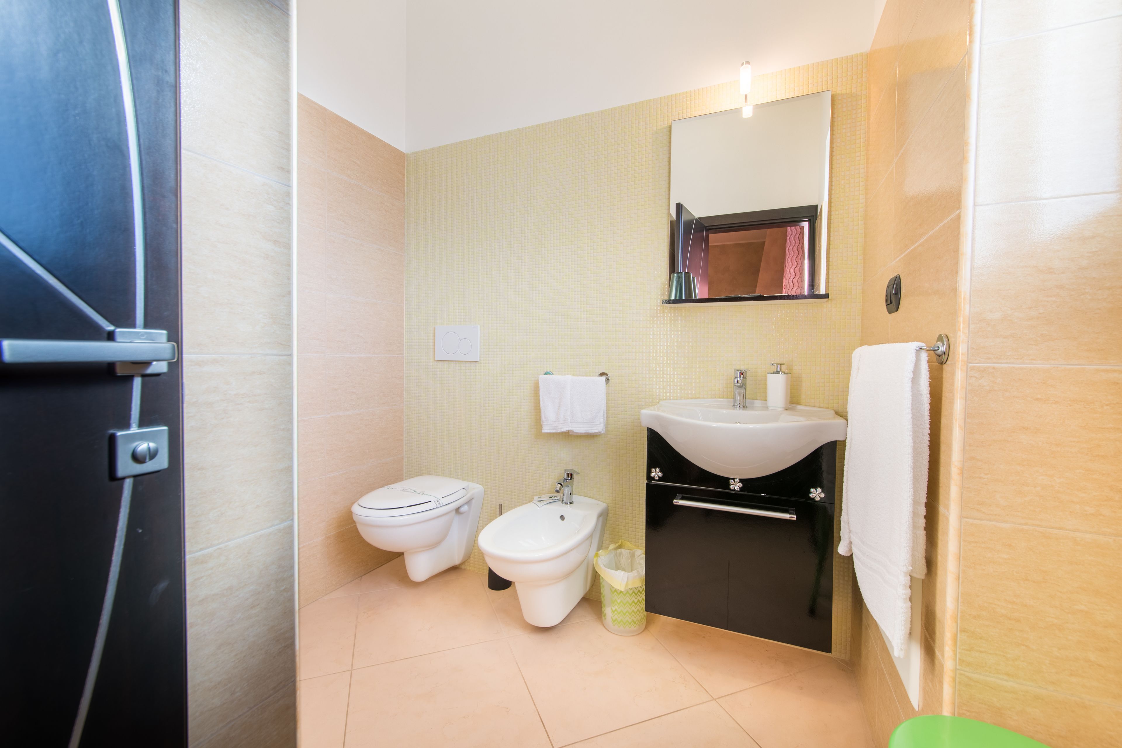 A bathroom with a toilet, bidet, sink, and mirror.