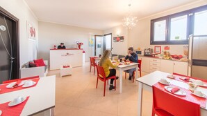 Un comedor con mesas dispuestas para dos, una recepción y una zona de cocina.