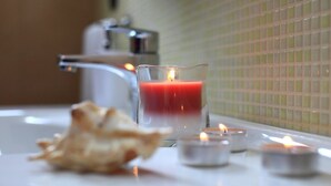 Un baño con un candelabro de vidrio que contiene una vela roja, una vela pequeña y una concha marina sobre el mostrador.