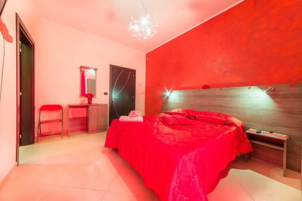 A modern bedroom with a red bedspread, a wooden headboard, and a small bedside table.