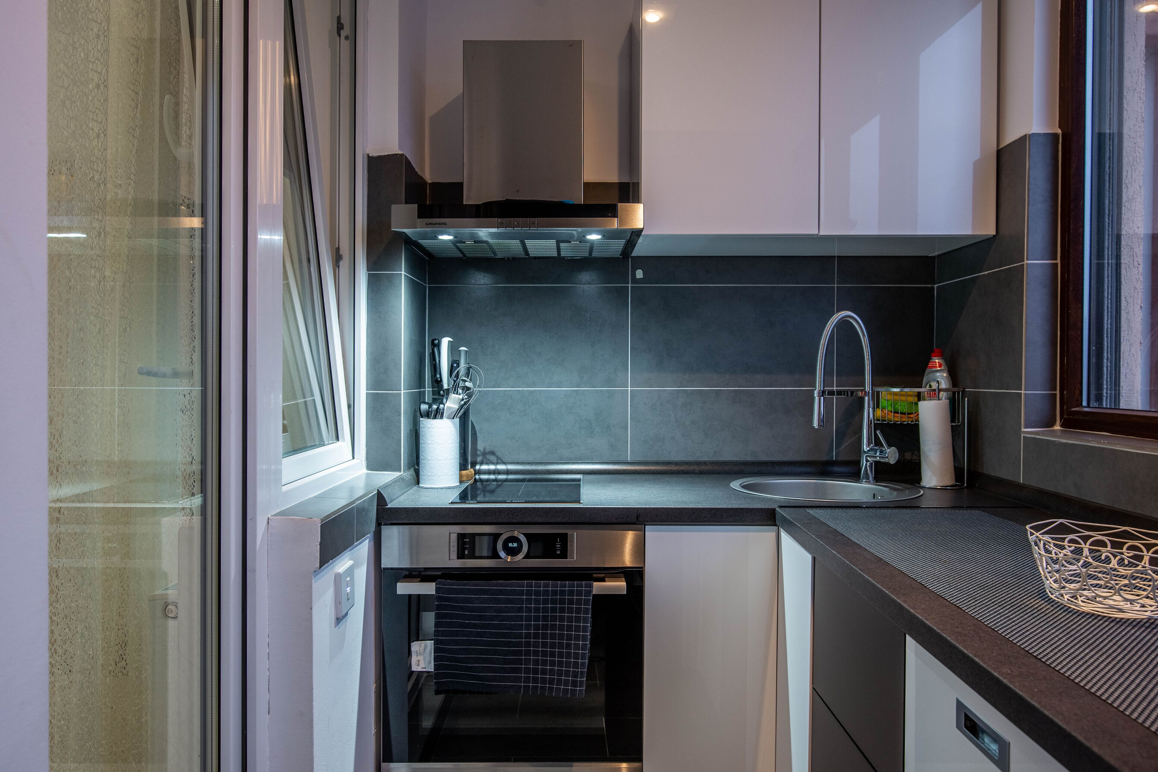 Cocina compacta con lavavajillas integrado, pileta de acero inoxidable y ventana que proporciona luz natural.