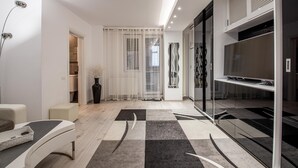 A modern living room with a sofa, a TV on a glass cabinet, a decorative vase, and a patterned rug. - Studio Militari Residence M2 (Chiajna)