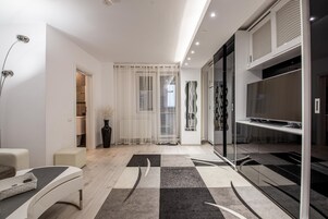 Una sala de estar moderna con un sofá, un televisor sobre un mueble de vidrio, un jarrón decorativo y una alfombra estampada.