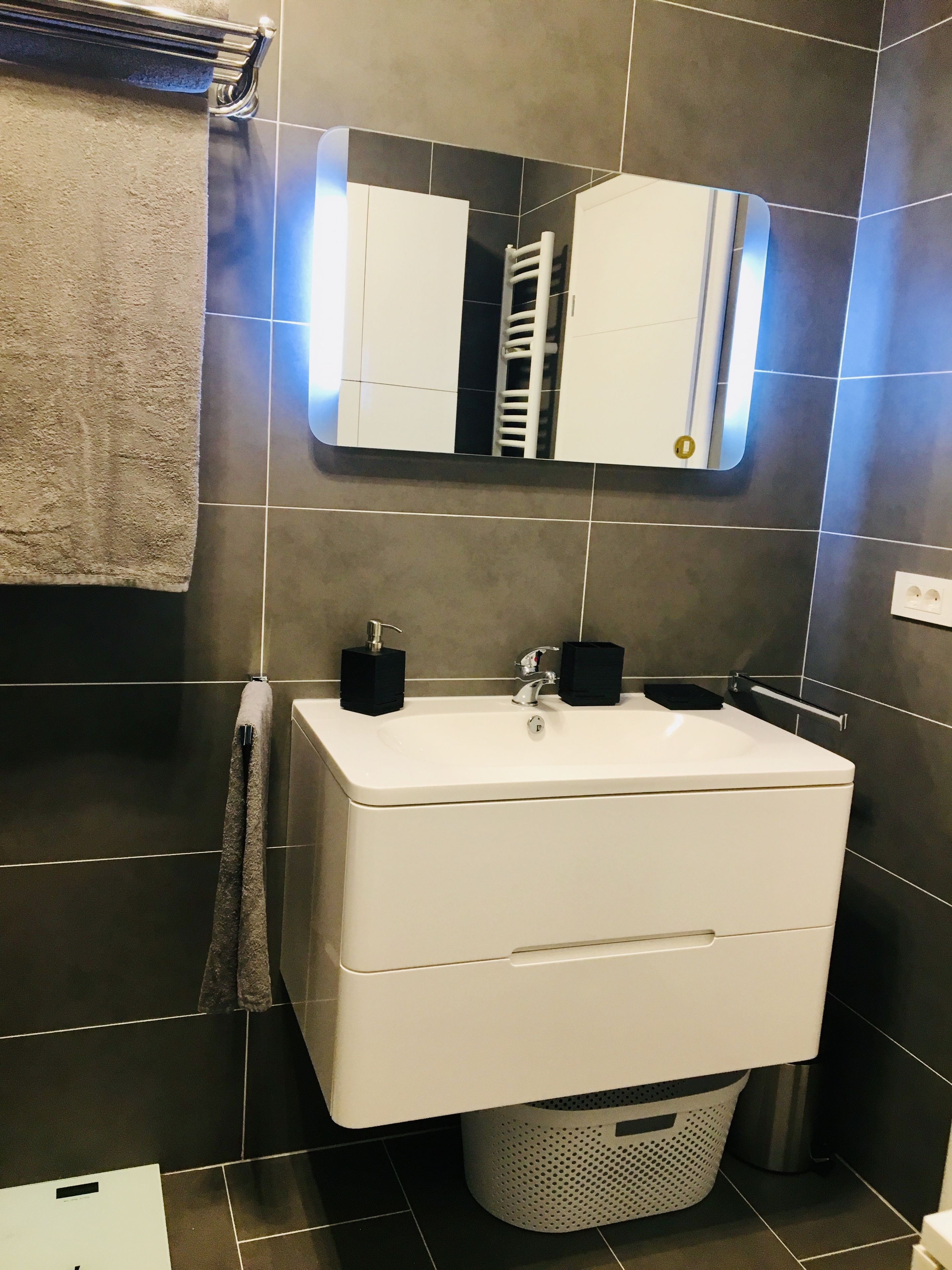 Une salle de bain moderne avec un lavabo blanc, un porte-serviettes, un miroir et une serviette accrochée au mur.