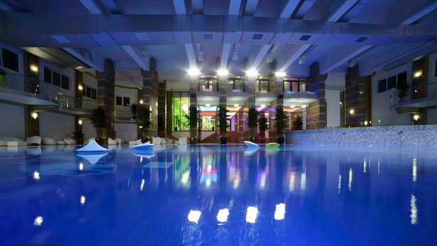 An indoor swimming pool with clear water, surrounded by a modern building with multiple floors and balconies. - Studio Militari Residence M2 (Chiajna)