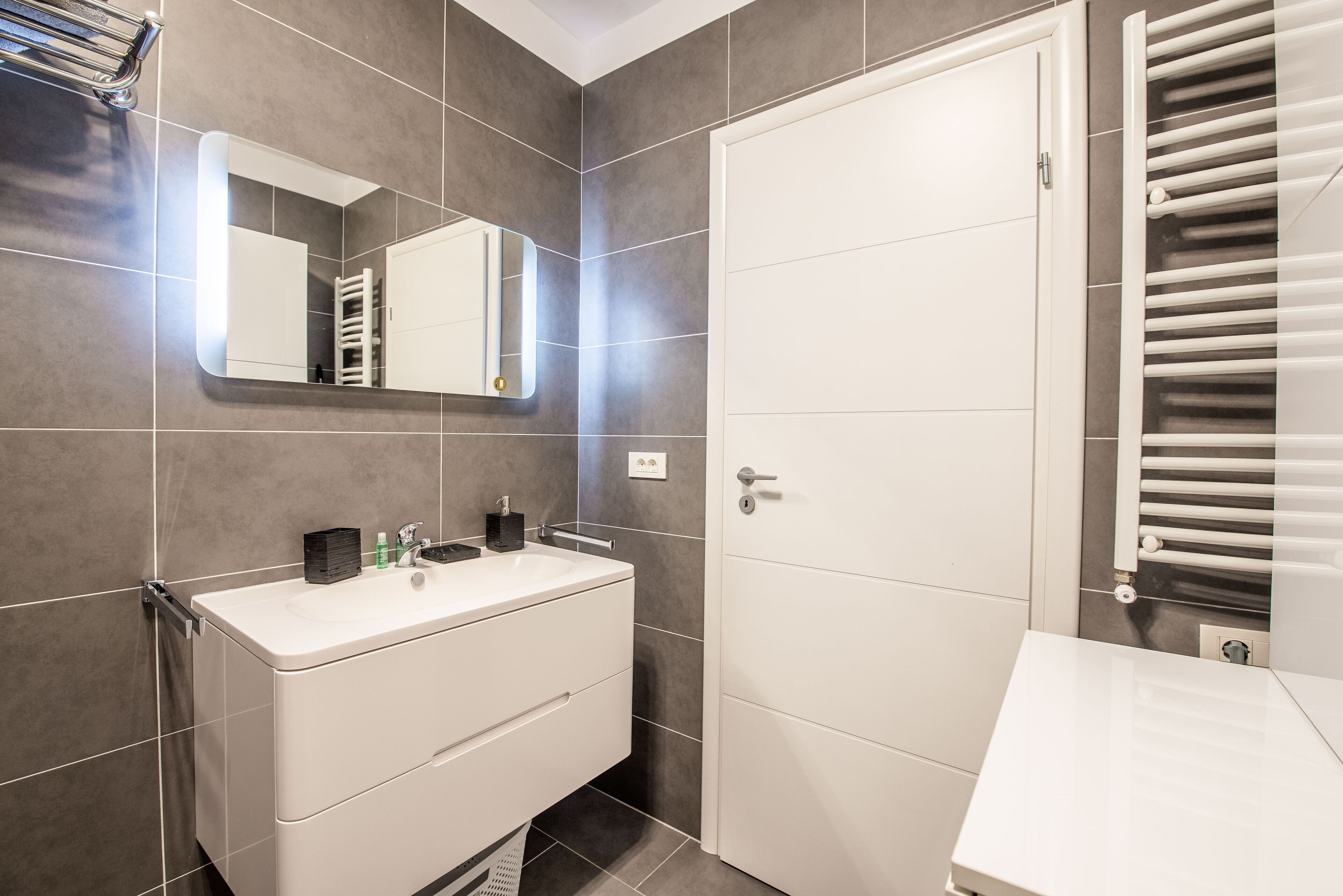 A modern bathroom with a white vanity, a mirror, and a towel rack.