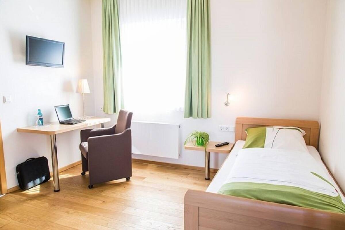 Hotelkamer met een bed, een bureau met een laptop, een stoel, een televisie en een raam met gordijnen.