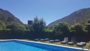 Une piscine rectangulaire à l’eau d’un bleu limpide, entourée d’une pelouse et d’arbres. Plusieurs chaises longues sont disposées le long du bord de la piscine.