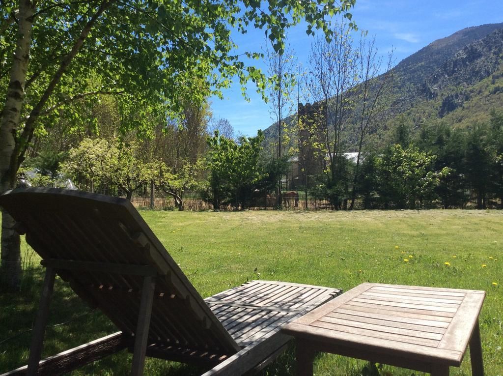 Una silla de madera y una mesa en un área cubierta de pasto, con montañas al fondo.