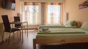 Ein Hotelzimmer mit zwei Betten, einem Schreibtisch mit Stuhl, einem an der Wand montierten Fernseher und einem Fenster mit Vorhängen.