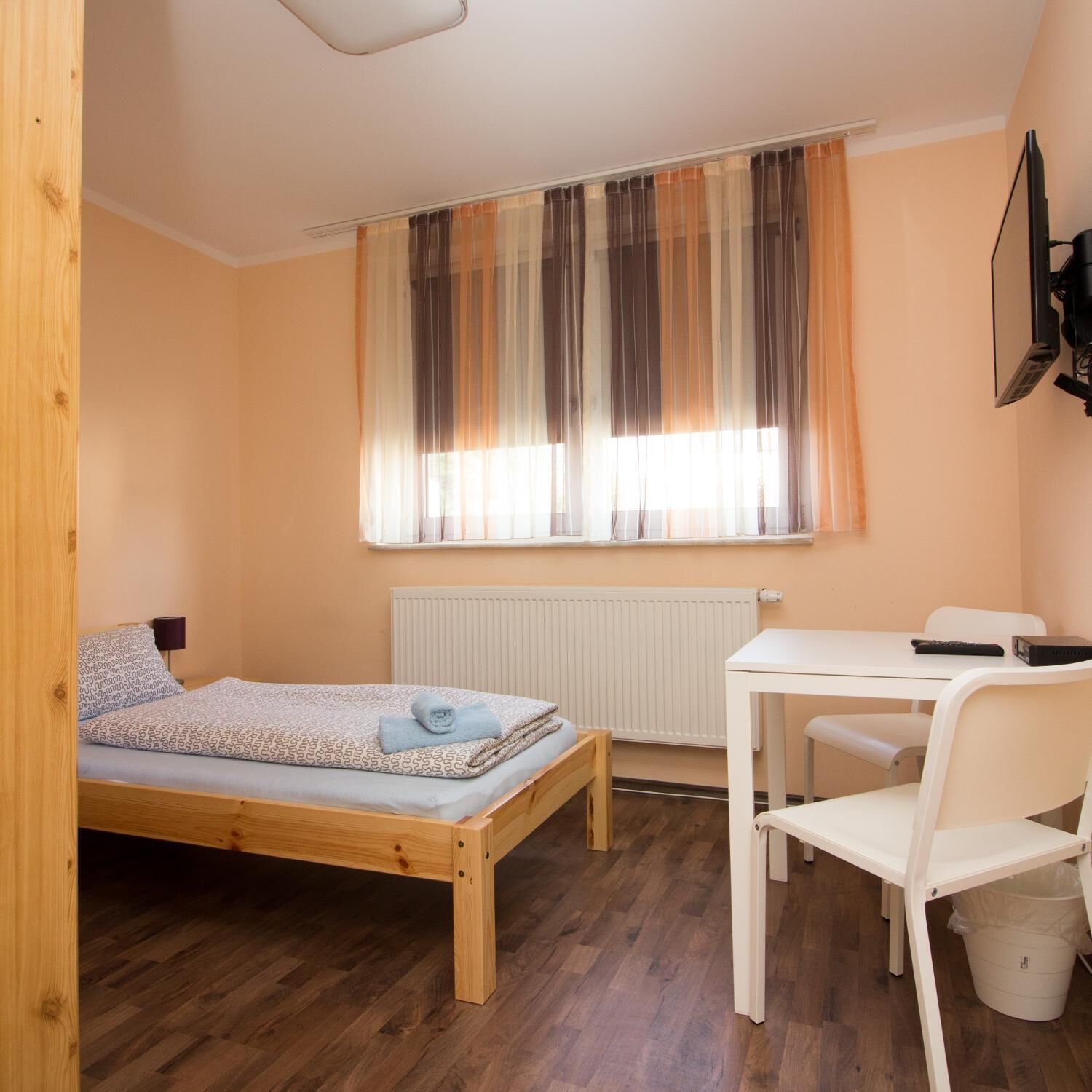 A small room with a wooden bed, a white desk, a chair, and a radiator.
