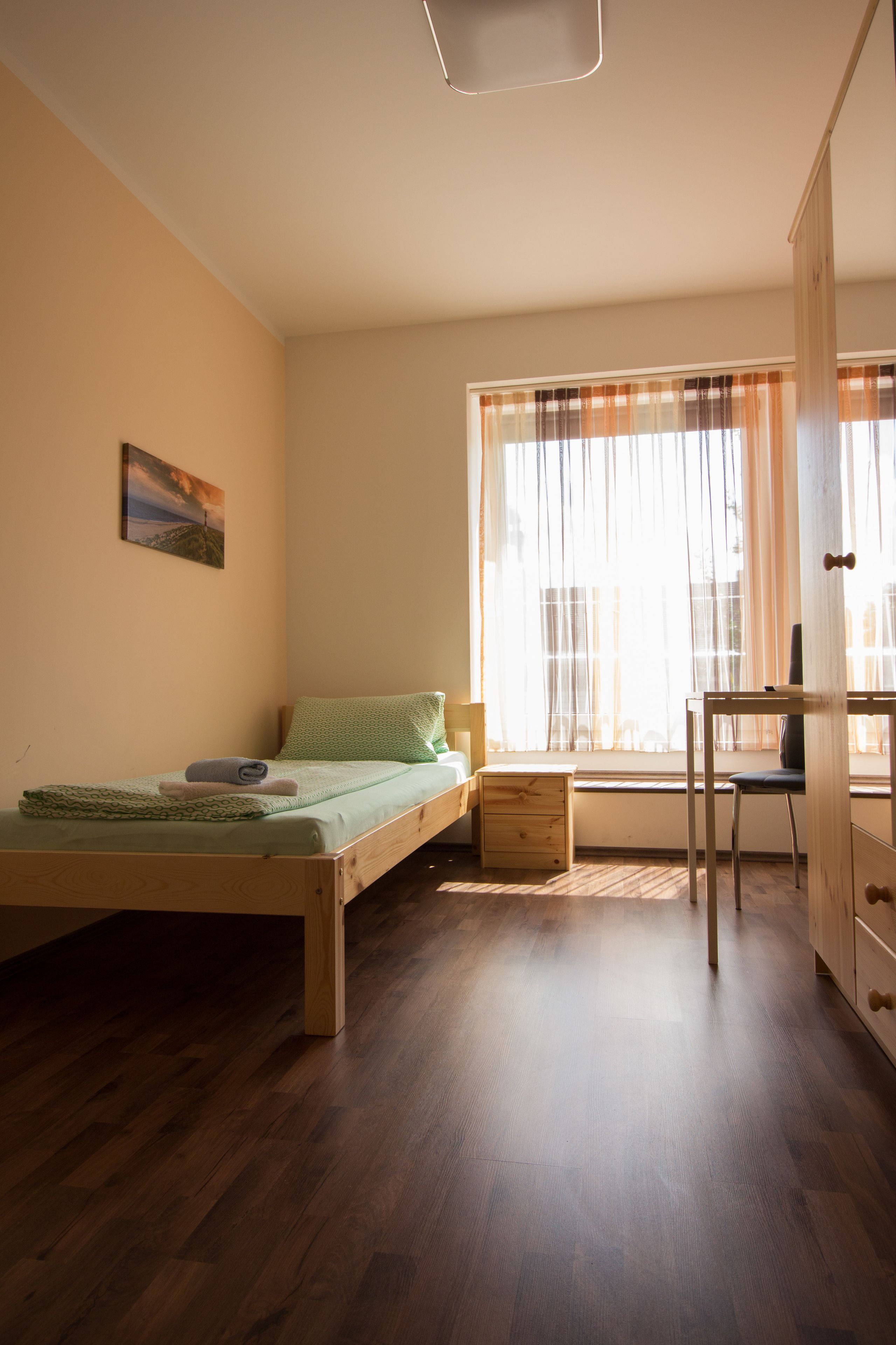 Une petite chambre avec un lit simple, un plancher en bois, un bureau et une chaise.
