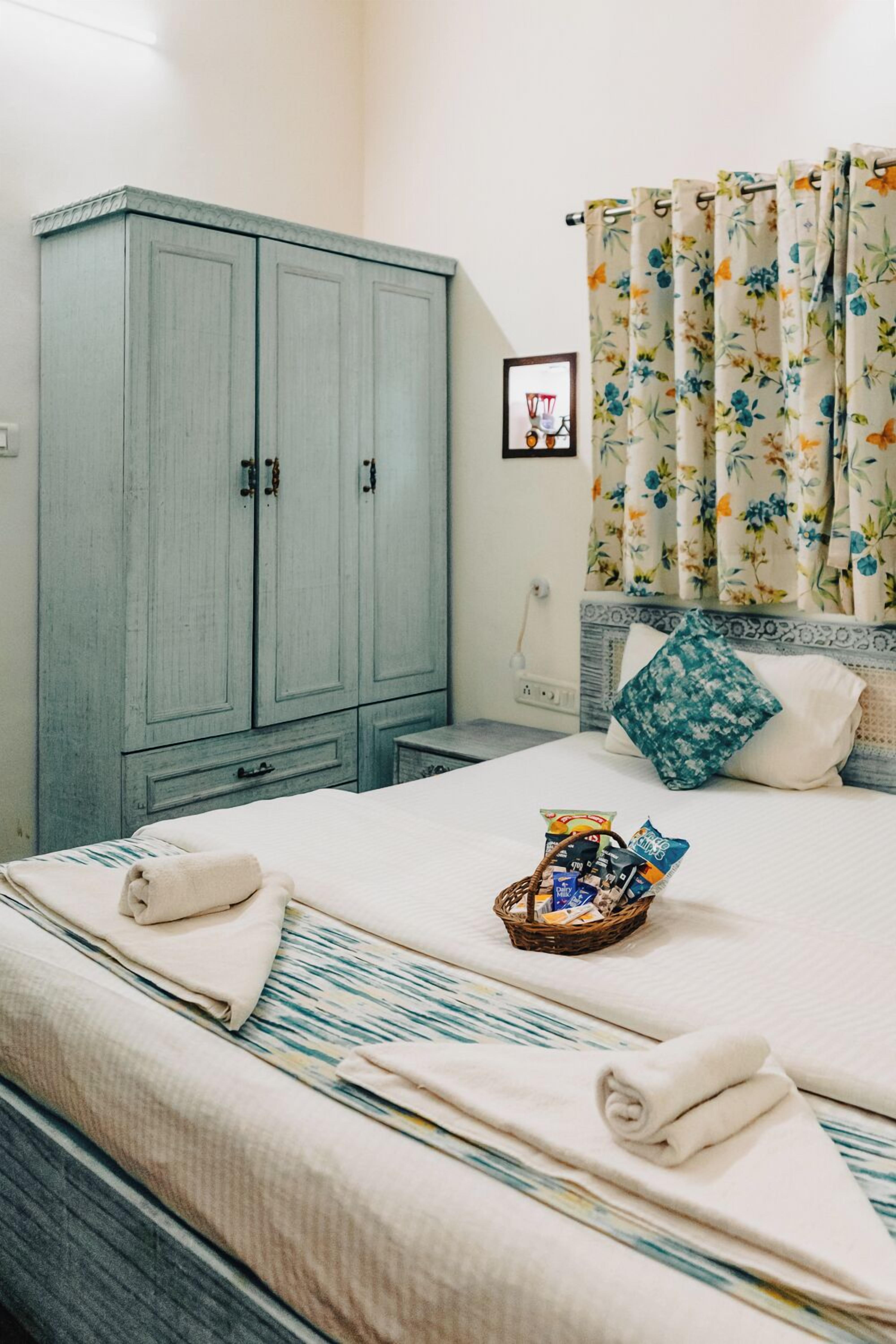 A neatly made bed with towels, a basket of snacks, and a floral curtain.
