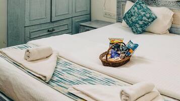 A neatly made bed with towels, a basket of snacks, and a floral curtain.