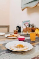 A breakfast setting with a plate of fried eggs, toast, and a pink cup, likely containing coffee or juice, on a table with a glass of orange juice.