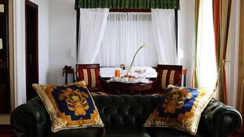 Quarto com sofá de couro preto, duas almofadas decorativas, mesa de jantar posta para o café da manhã e janela com cortinas brancas.