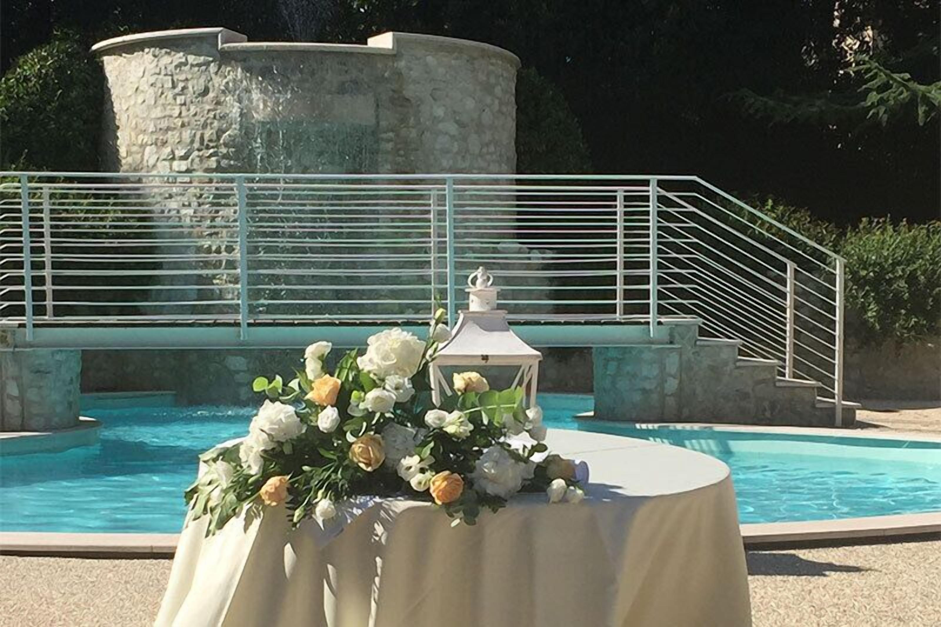 A pool area with a table set for a wedding, a white lantern, and a stone structure in the background.