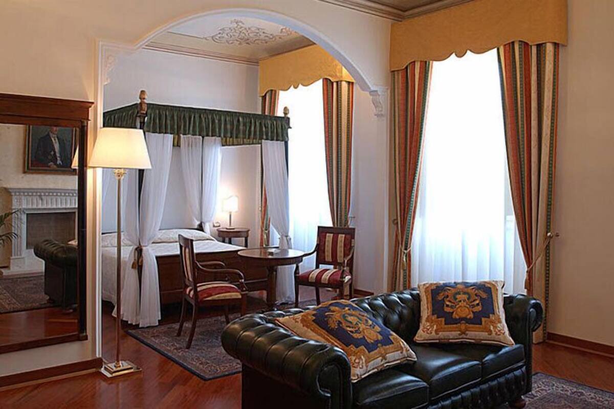 A hotel room with a bed, a sitting area with a sofa and armchairs, a small table, and a lamp.
