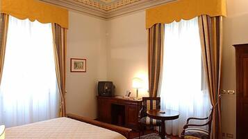 A hotel room with a bed, a desk with a lamp, a chair, and curtains.