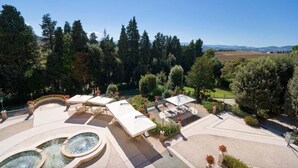 Un patio ajardinado con mobiliario exterior, una fuente y vistas a una zona boscosa.