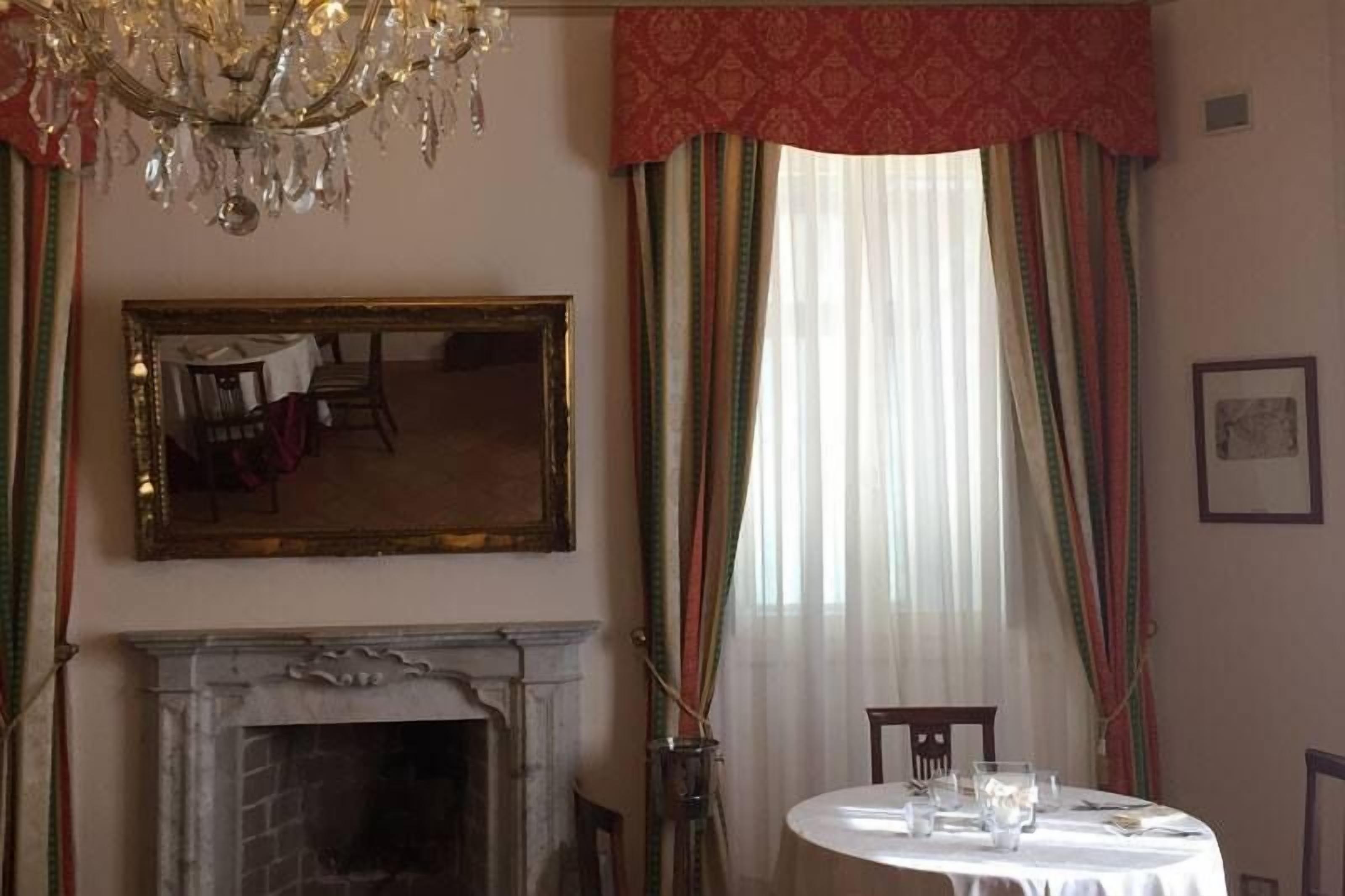 Un comedor con chimenea, un candelabro, una mesa redonda dispuesta para comer y un espejo grande en la pared.