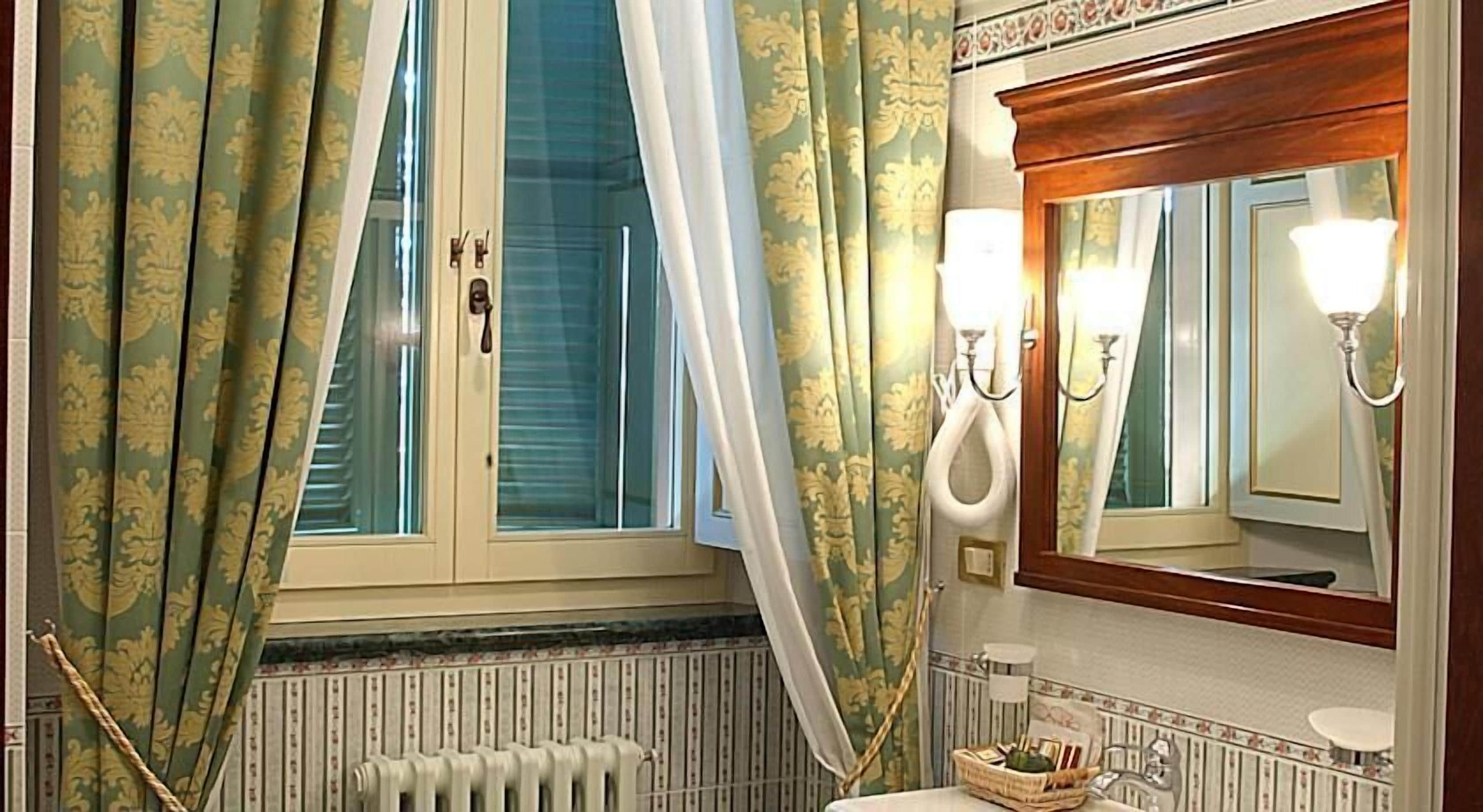 Une salle de bain avec une fenêtre, un radiateur, un lavabo et un miroir.
