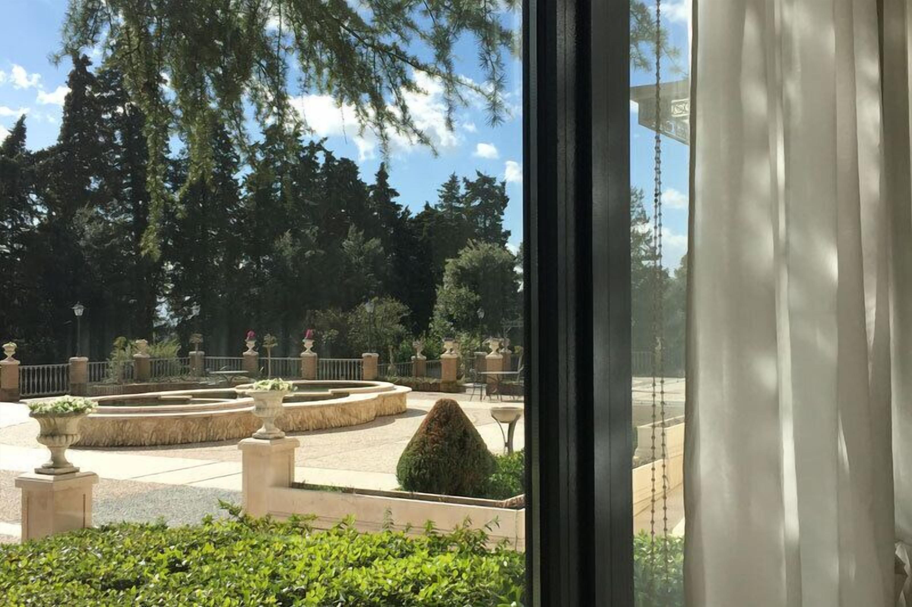 Vista de un jardín ajardinado con una fuente circular, rodeada de macetas de piedra y setos podados.
