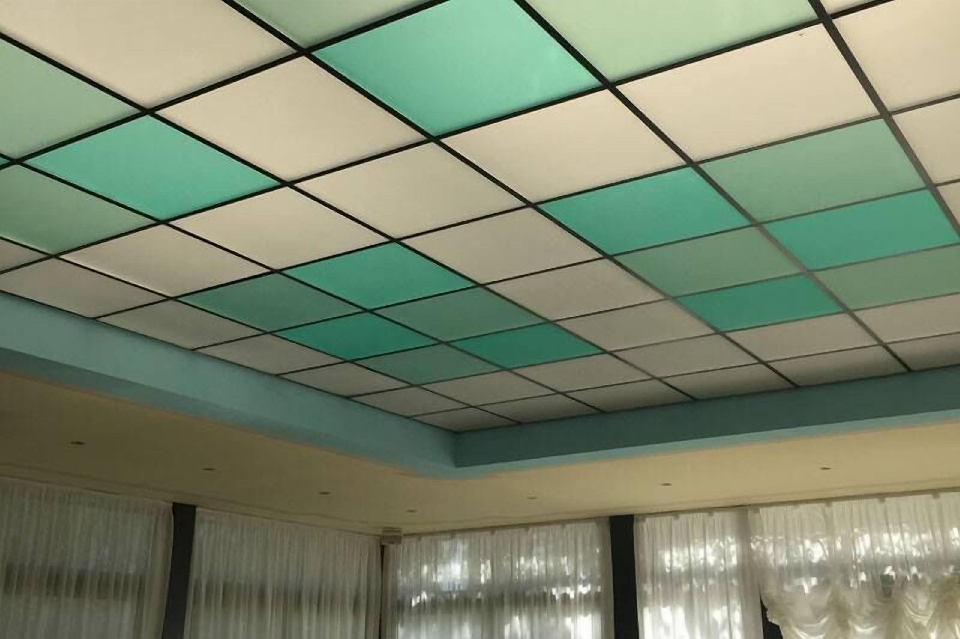 Une pièce avec un plafond à motifs géométriques, de grandes fenêtres ornées de rideaux légers et un mur sobre.