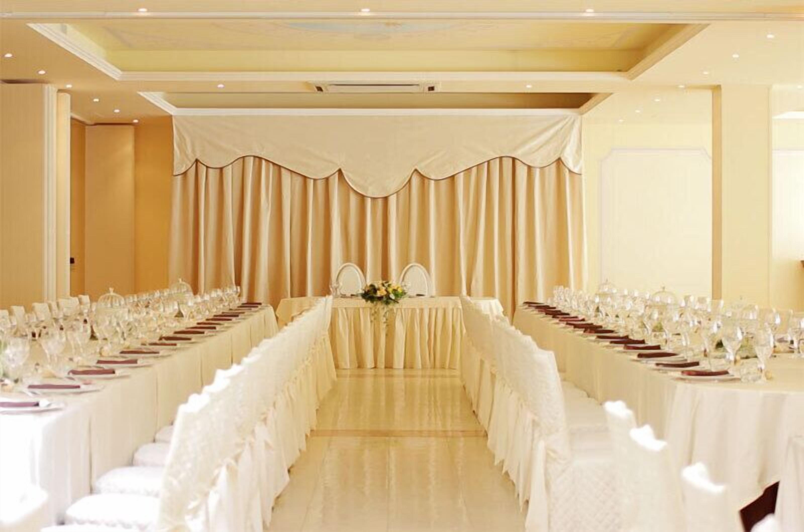 Una sala da banchetto con un lungo tavolo imbandito per un evento formale, affiancata da tende e sedie.
