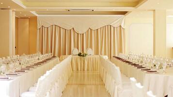 Una sala da banchetto con un lungo tavolo imbandito per un evento formale, affiancata da tende e sedie.