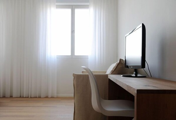A minimalist office space with a wooden desk, a modern monitor, and a white chair. - Pianderna Agriwellness (Scandiano)