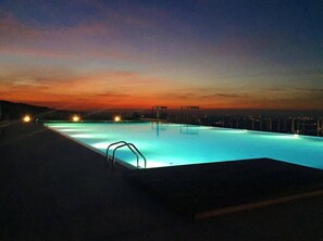 A swimming pool at dusk with city lights in the background.