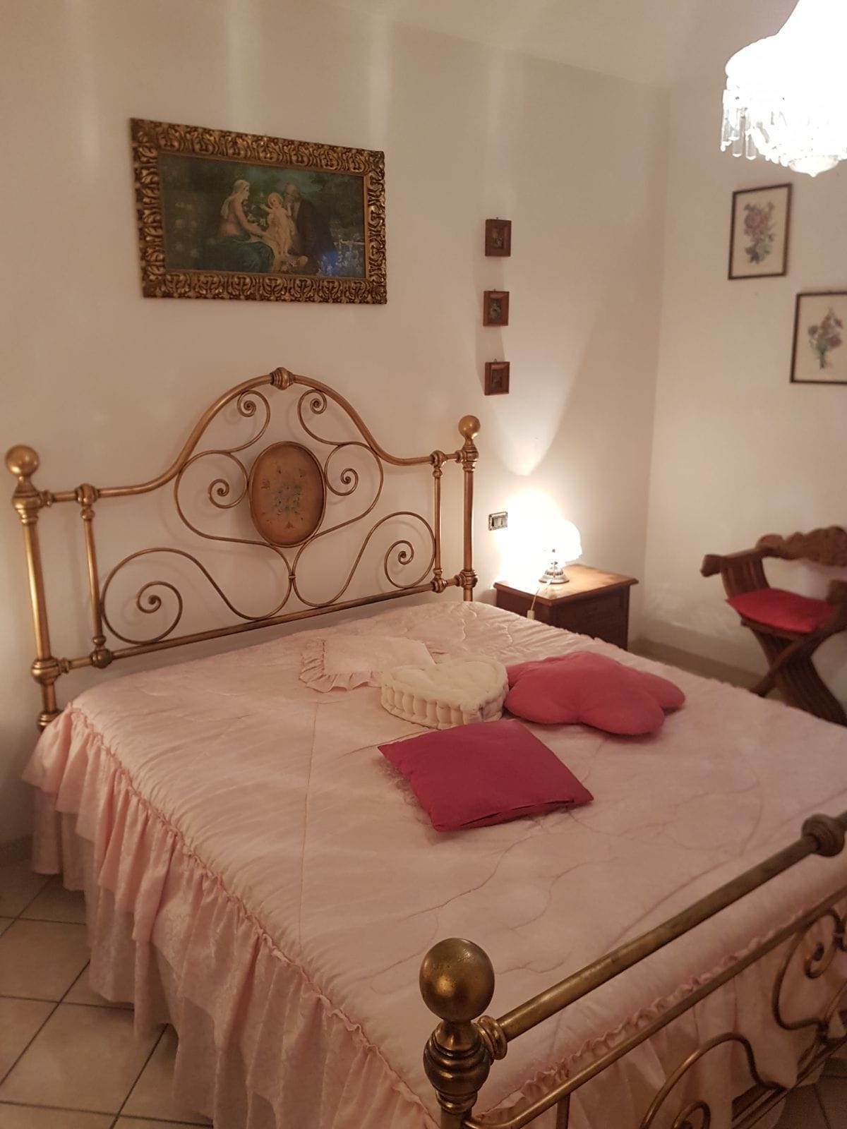 Un dormitorio con estructura de cama metálica, colcha rosa y un espejo decorativo.
