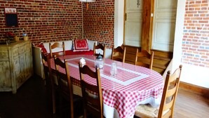 Un comedor con pared de ladrillo, una mesa de madera con mantel a cuadros y sillas de madera.