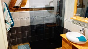 Un baño con ducha de azulejos negros, lavabo blanco y tocador de madera.