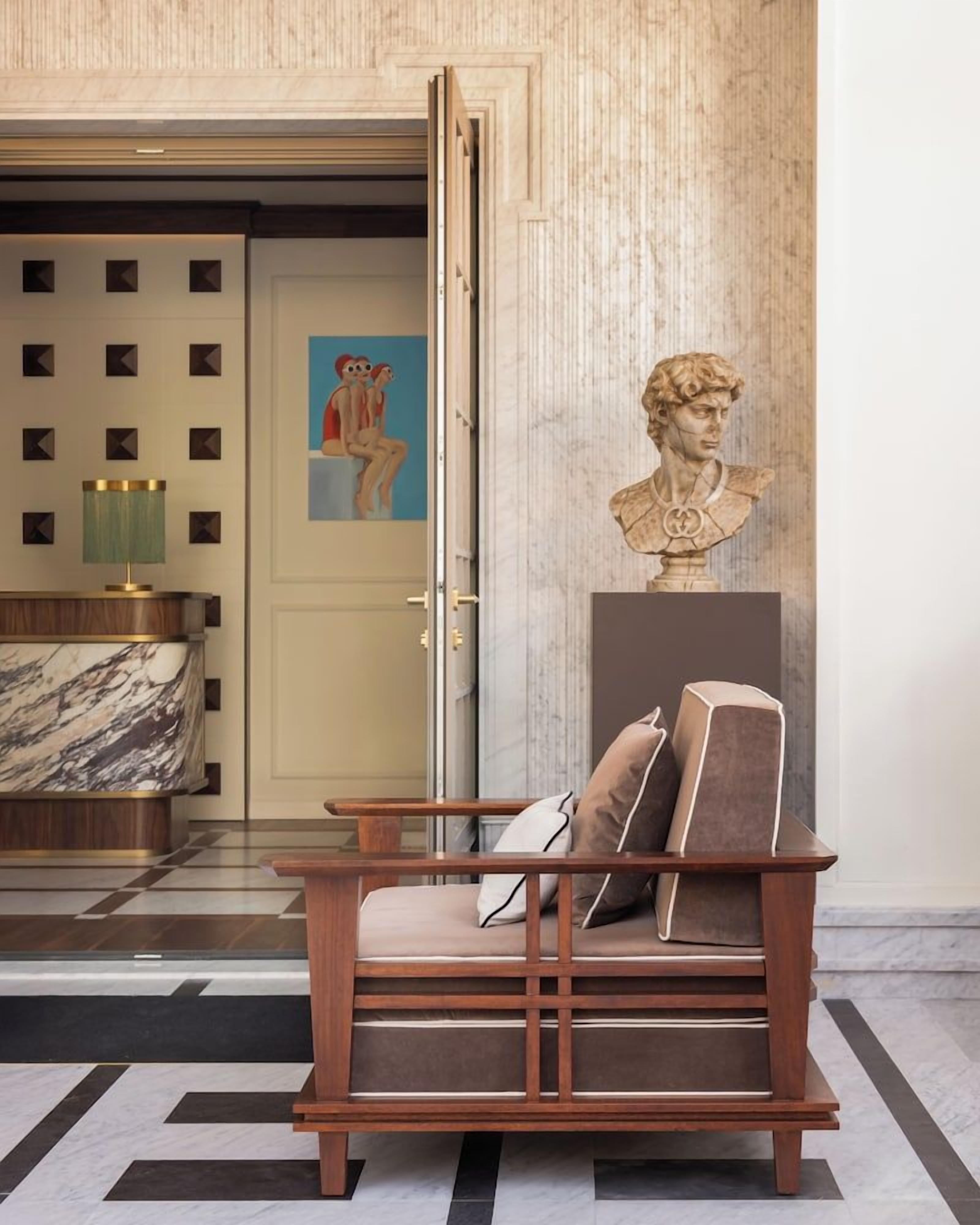 Um hall de entrada com uma recepção de mármore, um banco de madeira com almofadas, um busto e um quadro na parede.