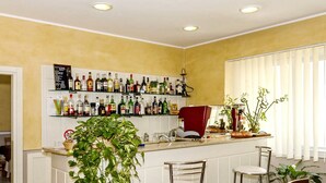 A bar area with a white counter, multiple liquor bottles, and two bar stools. - Hotel Nautilus (Forte dei Marmi)