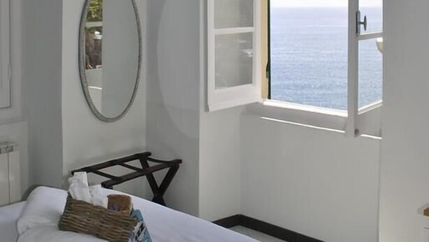 A bedroom with a bed, a bedside table, a mirror, and a window with a view of the sea. - Al Piccolo Scoglio - Room & Breakfast (Camogli)