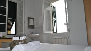 A hotel room with a bed, a sink, a mirror, a window with shutters, and a radiator. - Al Piccolo Scoglio - Room & Breakfast (Camogli)