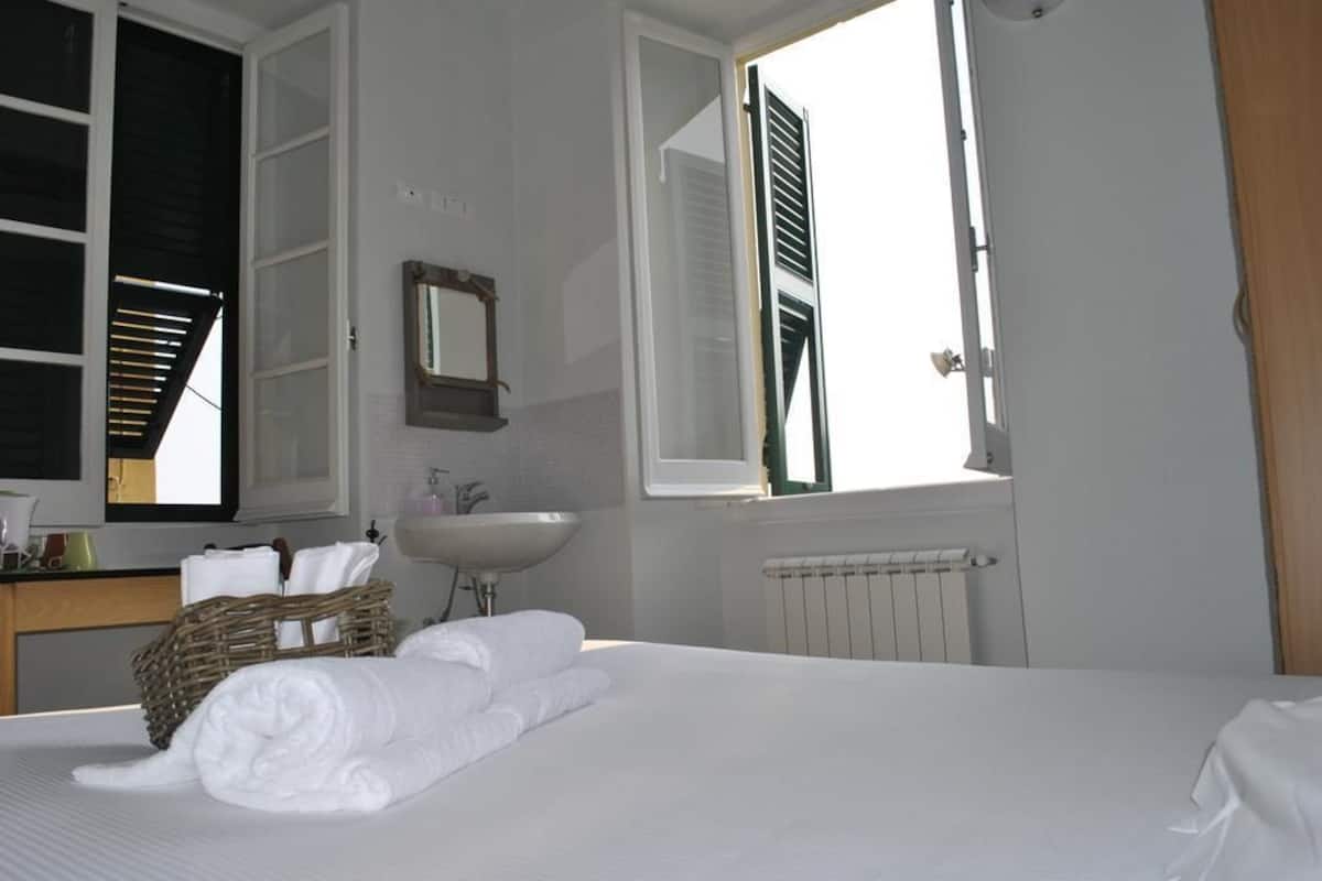 A hotel room with a bed, a sink, a mirror, a window with shutters, and a radiator.