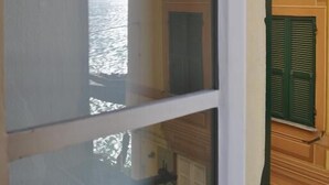 A room with a large window overlooking a body of water, a wooden wall, and green shutters. - Al Piccolo Scoglio - Room & Breakfast (Camogli)