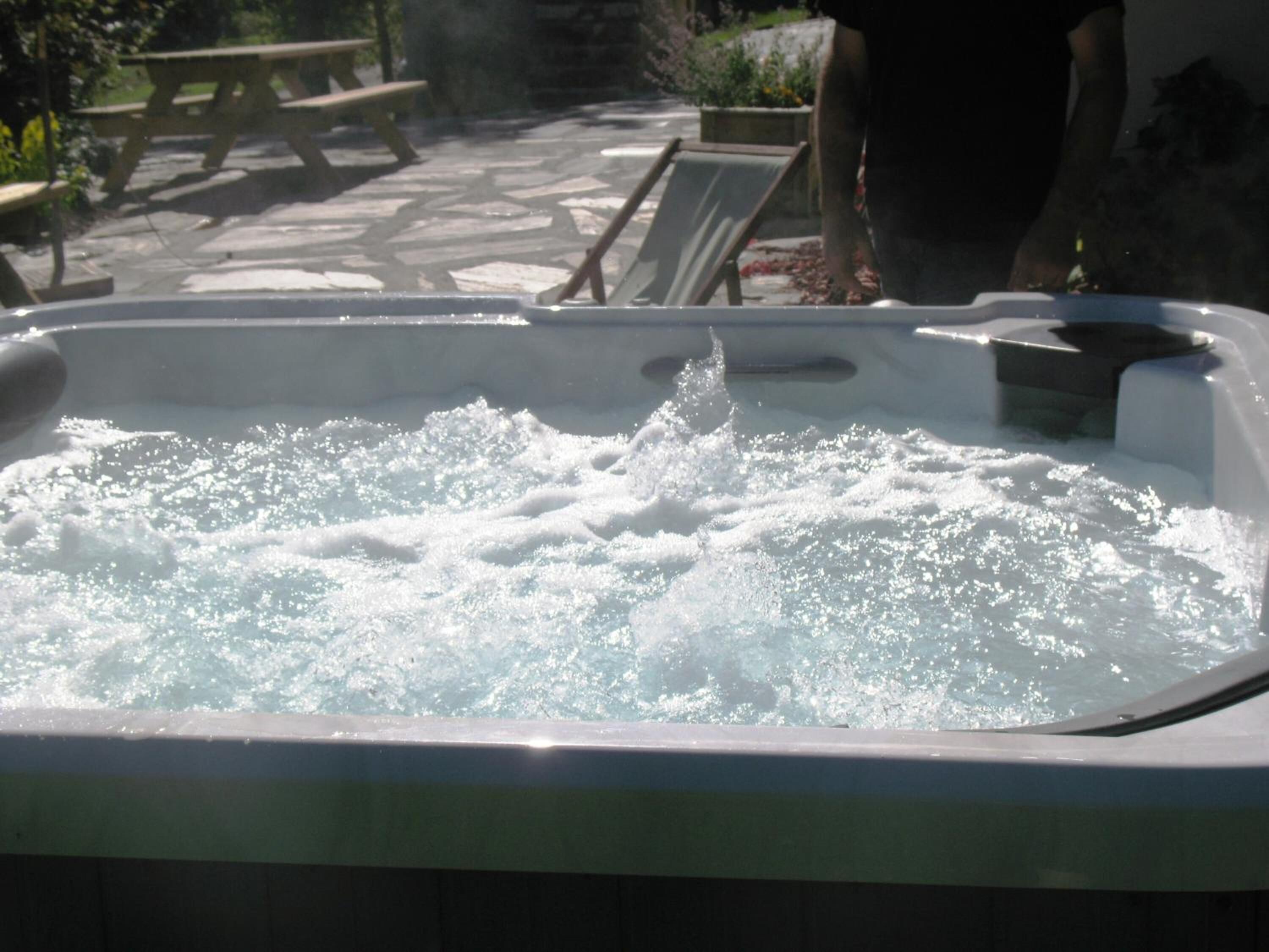 A hot tub with water jets, surrounded by outdoor furniture and a stone patio.