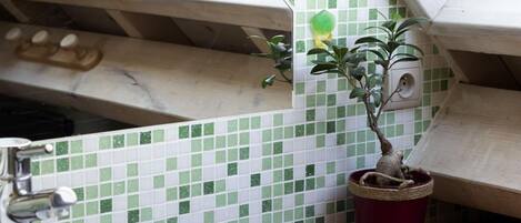 A bathroom with a white sink, green and white tiled backsplash, and a potted plant.