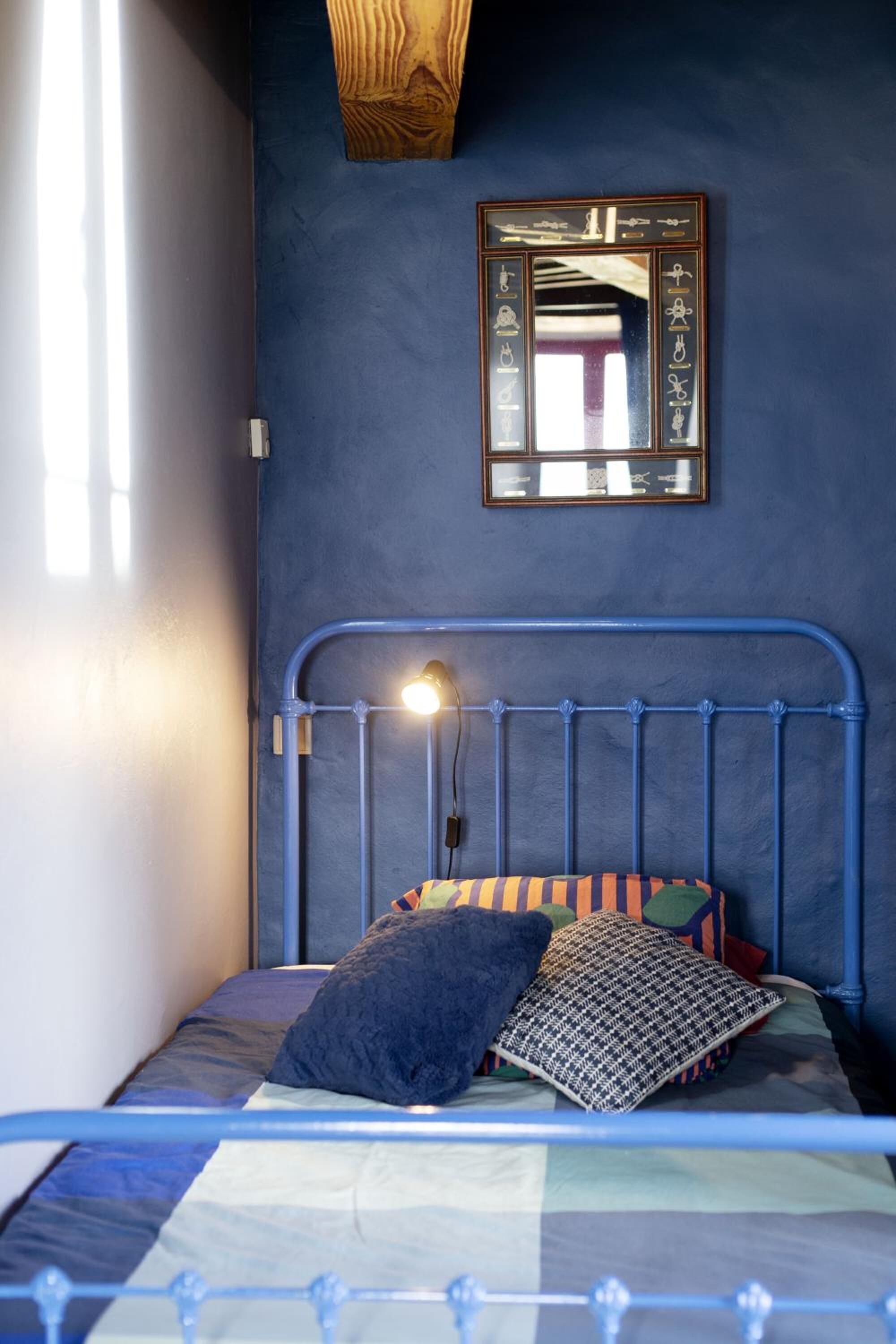 Ein Schlafzimmer mit einem blauen Metallbettgestell, einer Nachttischlampe und einem an der Wand befestigten Spiegel.