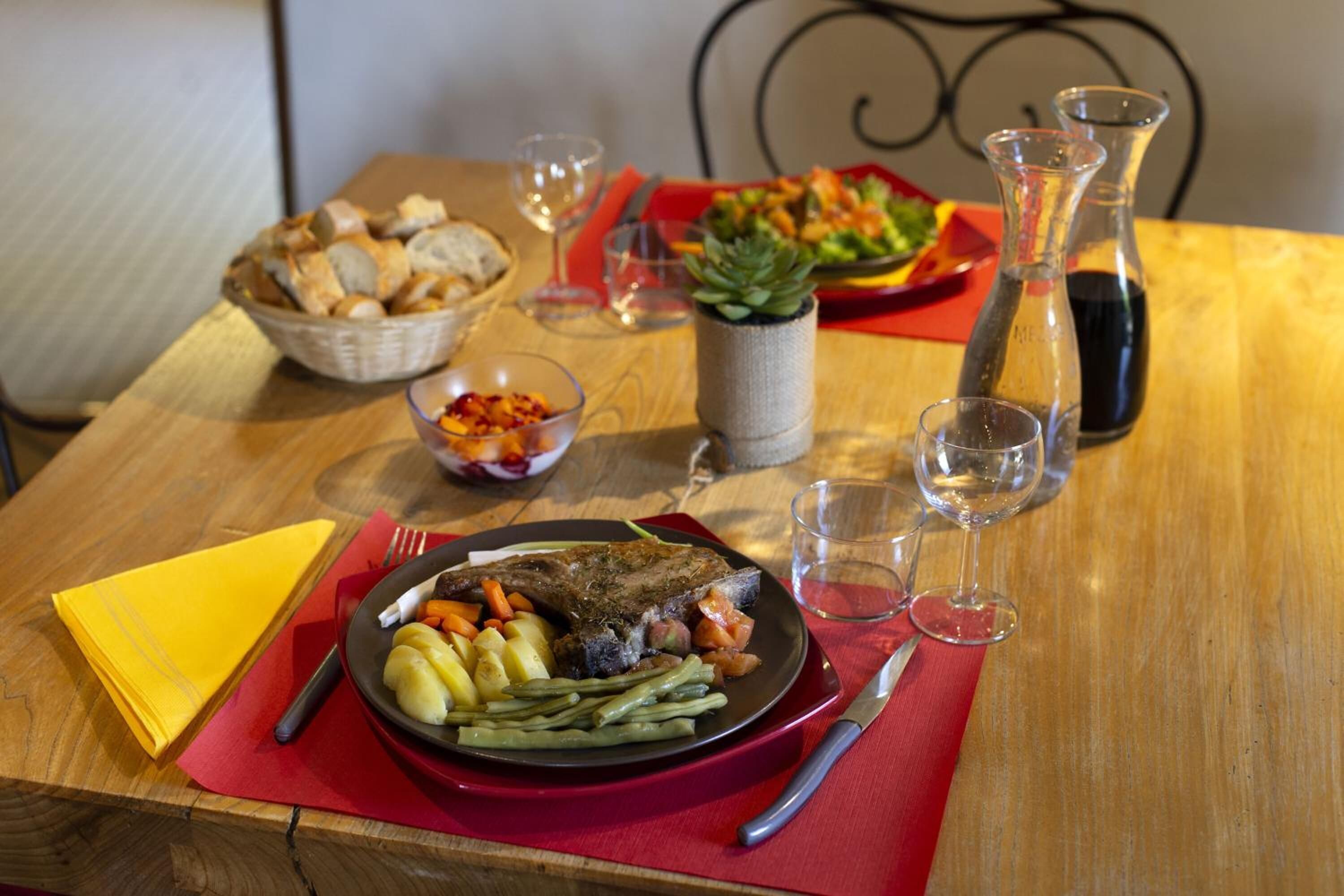 A wooden dining table with a plate of food, including a steak, potatoes, and green beans, and a basket of bread.