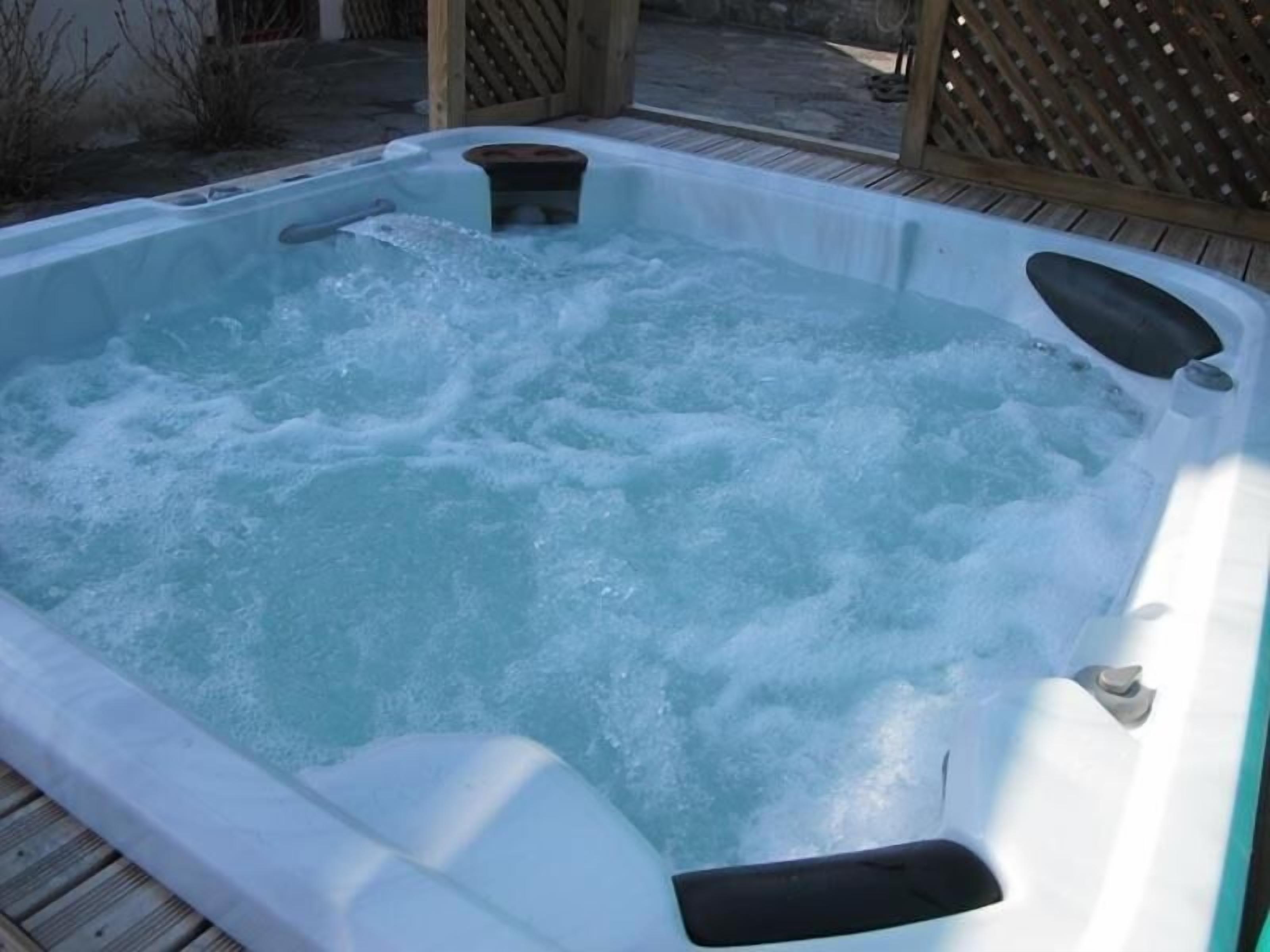 Un bain à remous équipé de jets d’eau, entouré d’une terrasse en bois et d’une clôture en bois.