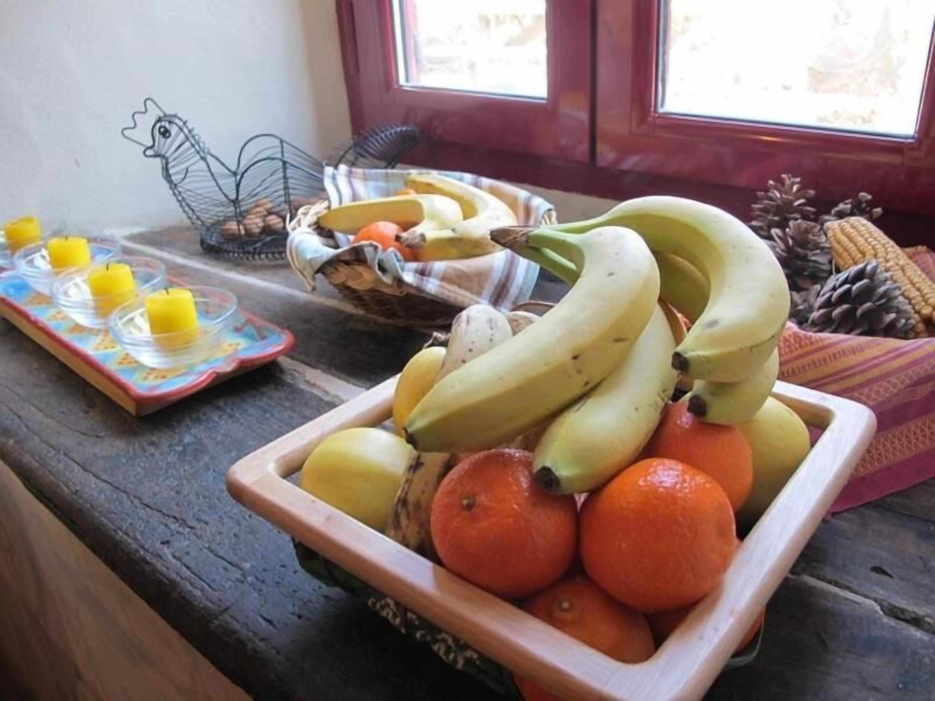 A kitchen counter with a fruit bowl containing bananas and oranges, a wire basket with bread, and a small tray with candles.