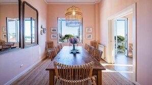 Ein Esszimmer mit Holztisch, Korbstühlen, einem Chandelier und großen Fenstern mit Blick ins Freie.