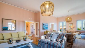 Ein modernes Wohnzimmer mit einer Couch, einem Couchtisch und einem gestreiften Ohrensessel. Zwei Pendelleuchten und ein großes Fenster sind vorhanden.
